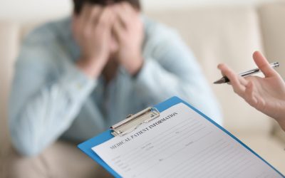Depressed guy visiting doctor, having complaints about health or mental problems. Focus on doctors hand holding clipboard with patient card, psychologist starts working with troubled man. Close up