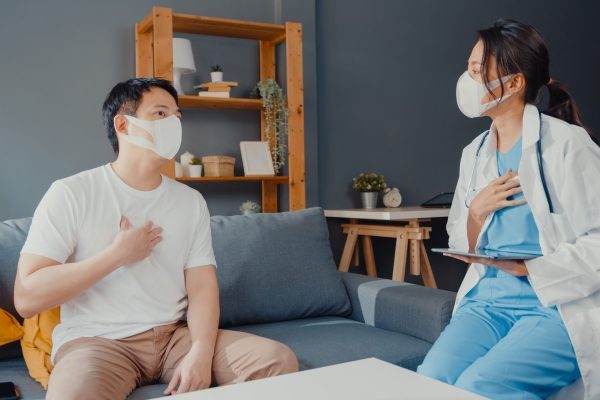 young-asia-female-physician-doctor-wear-face-mask-using-digital-tablet-sharing-good-health-test-news-with-happy-male-patient-sit-couch-house-scaled